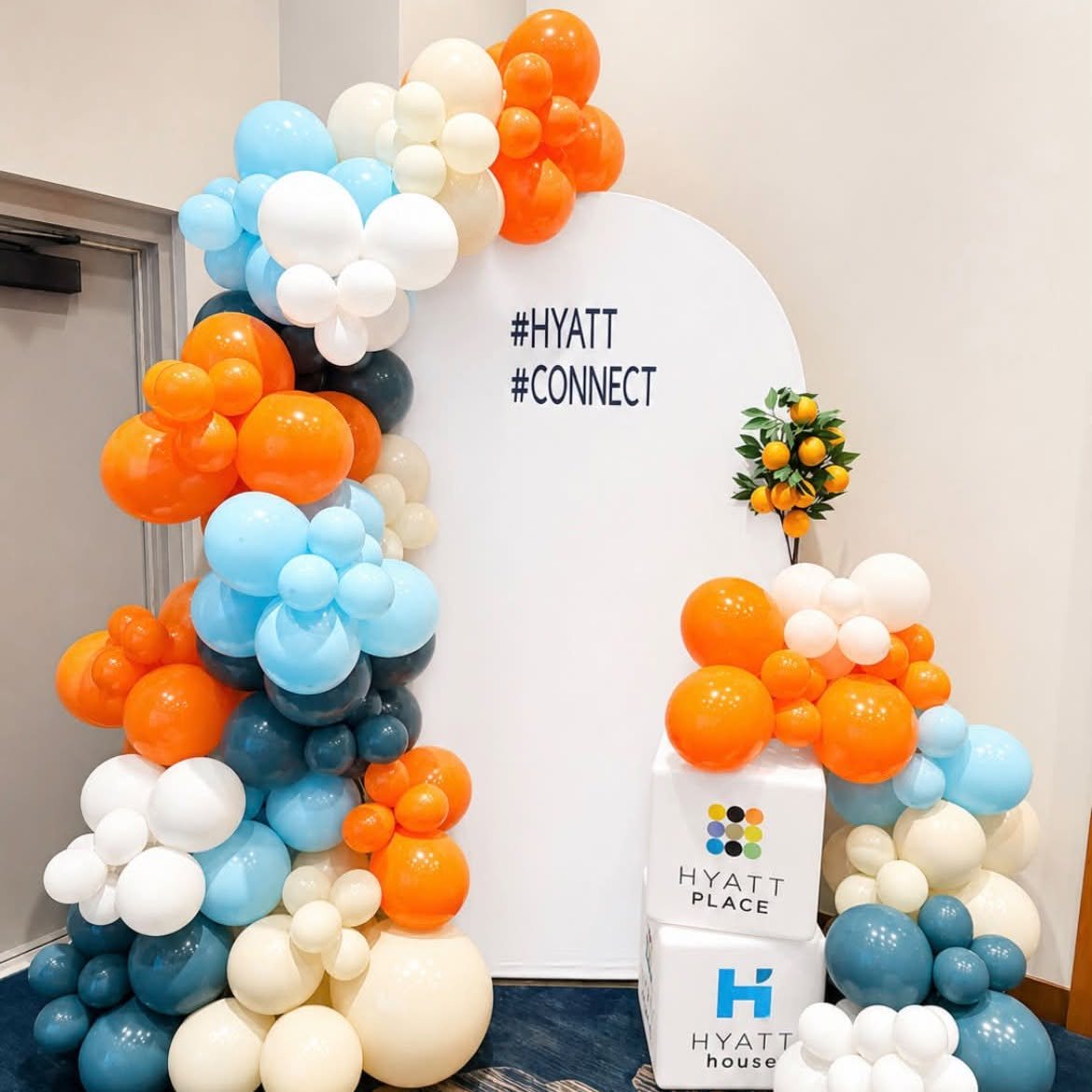 Orange, blue and cream balloon arch beside a Hyatt Place branded backdrop