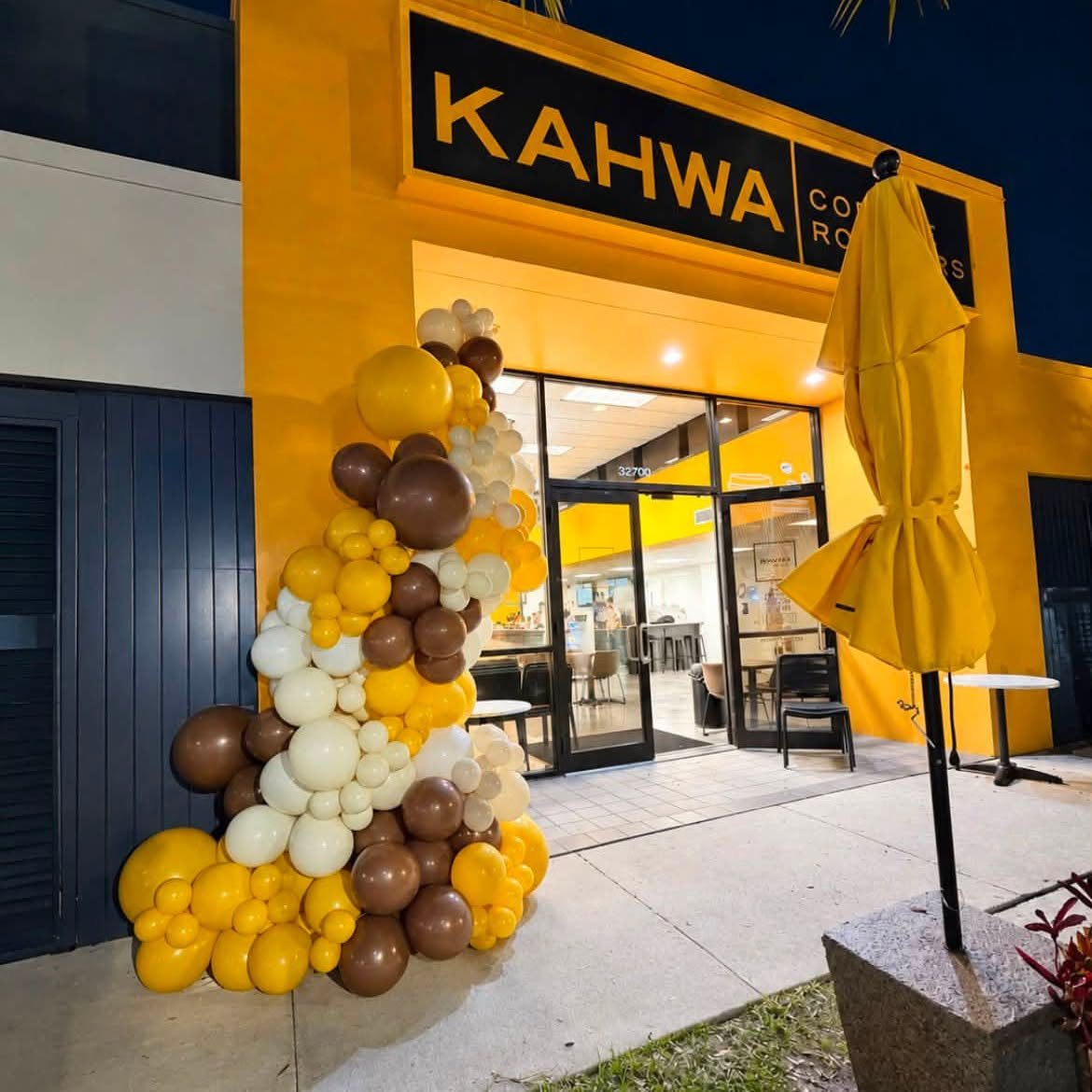 Yellow, brown and cream balloon garland climbing the yellow storefront of Kahwa Coffee at night