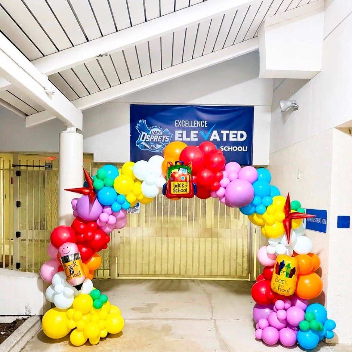Full rainbow balloon arch with Back to School foil balloons over a school entrance