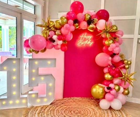 Pink and gold balloon arch with a Happy Birthday neon sign and lit marquee number 15